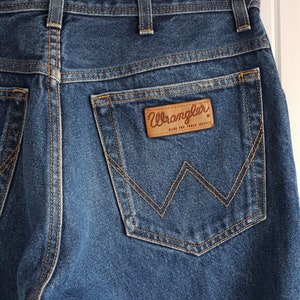 May include: A pair of blue denim jeans with a back pocket featuring a brown leather Wrangler label with the text "Wrangler Made for Tough Service".