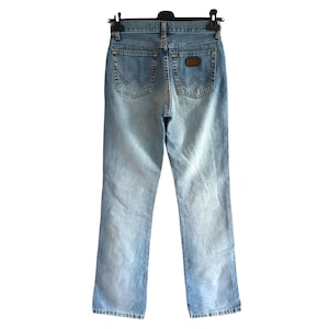 May include: Light blue denim jeans with a classic five-pocket design. The jeans feature a faded wash and a brown leather patch on the back. The jeans are hanging on a black hanger.