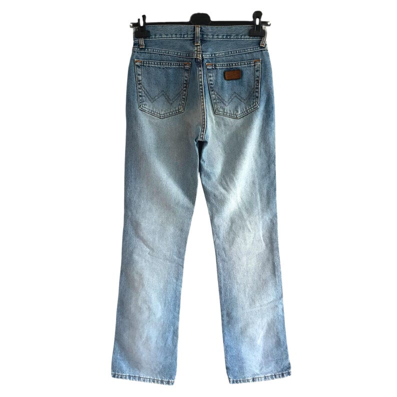 May include: Light blue denim jeans with a classic five-pocket design. The jeans feature a faded wash and a brown leather patch on the back. The jeans are hanging on a black hanger.