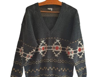 May include: A dark gray v-neck sweater with a geometric pattern in shades of beige, red, and black. The pattern is a repeating design of triangles and diamonds.