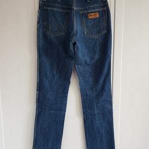 May include: A pair of blue denim jeans with a brown leather Wrangler label on the back pocket.