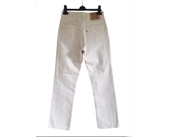 May include: Off-white denim jeans hanging on a black hanger. The jeans have a high waist and a straight leg. A brown leather patch is visible on the back waistband. The jeans are made of a sturdy denim material.