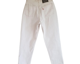 May include: Off-white denim jeans hanging on a black hanger. The jeans have a classic five-pocket design, with a red tab on the back pocket. A black and red label is visible at the back of the waistband.