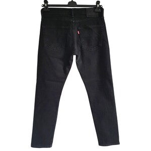 Könnte beinhalten: Schwarze Jeans aus Denim, die an einem schwarzen Kleiderbügel hängen. Die Jeans haben ein klassisches Fünf-Taschen-Design, einen Lederaufnäher und ein kleines rotes Etikett auf der Gesäßtasche. Die Jeans sind einfarbig schwarz.