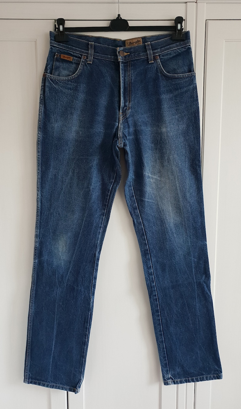 May include: A pair of blue denim jeans with a brown leather patch that says "Wrangler" on the back waistband.