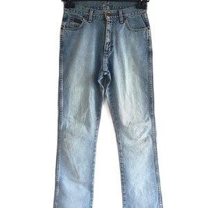 May include: Light blue denim jeans hanging on a black hanger. The jeans have a classic five-pocket design, a button and zipper closure, and a faded wash. The jeans are straight-legged and appear to be in good condition.