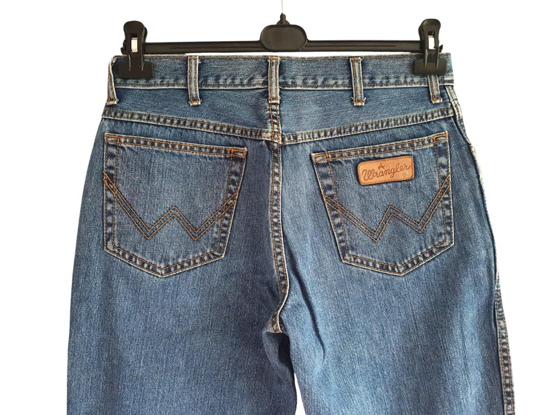 May include: A pair of blue denim jeans with a brown leather patch that says "Wrangler" on the back pocket.