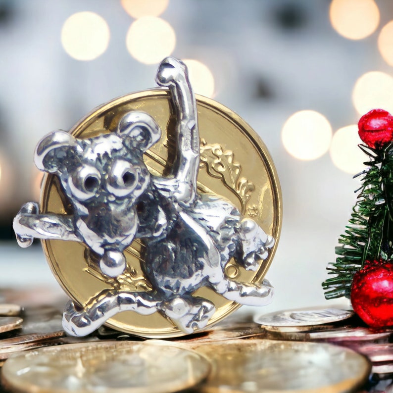 K&ouml;nnte beinhalten: Ein silberner Affen-Anh&auml;nger mit einer Goldm&uuml;nze dahinter. Der Affe h&auml;lt einen kleinen roten Ball in seiner Hand. Der Anh&auml;nger liegt auf einem Stapel Goldm&uuml;nzen.