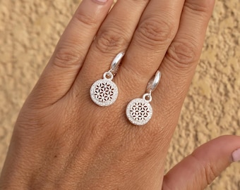 May include: Silver hoop earrings with a dangling charm featuring a detailed flower design.