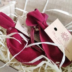 May include: Two red velvet pouches with a brown tag that says "Mia Silken Studio jewelry with stories". The pouches are sitting in a box filled with shredded paper.