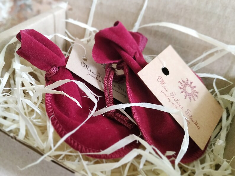 May include: Two red velvet pouches with a brown tag that says "Mia Silken Studio jewelry with stories". The pouches are sitting in a box filled with shredded paper.