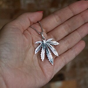 May include: A silver pendant necklace featuring a detailed marijuana leaf design.