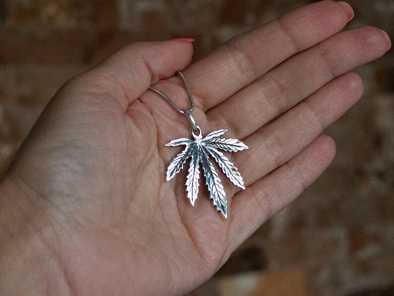 May include: A silver pendant necklace featuring a detailed marijuana leaf design.
