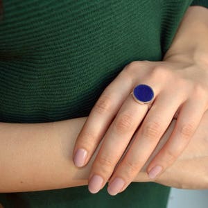 May include: A silver ring with a large oval blue gemstone. The ring is on a person's finger.
