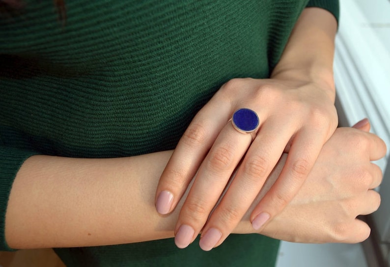 May include: A silver ring with a large oval blue gemstone. The ring is on a person's finger.