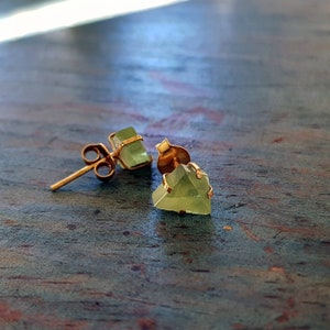 Op de afbeelding: Een paar gouden oorbellen met groene edelsteen driehoekige studs.