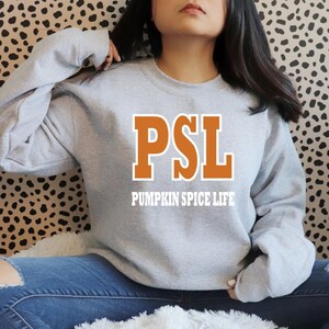 Peut inclure: Un sweat-shirt gris avec le texte "PSL Pumpkin Spice Life" en lettres orange et blanches.
