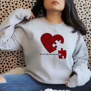 May include: A gray sweatshirt with a red heart-shaped puzzle piece design. The text "you are my missing piece" is printed below the heart.