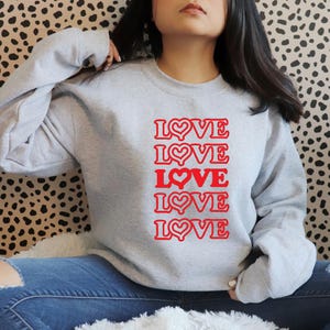 May include: A grey sweatshirt with the word "LOVE" repeated five times in red with a heart in each word. The hearts are outlined in red.