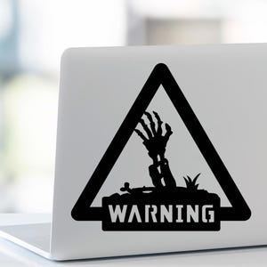 Puede incluir: Adhesivo en blanco y negro que presenta una señal de advertencia con una mano esquelética que emerge del suelo. La palabra "WARNING" se muestra en negrita, en mayúsculas, debajo de la mano dentro de un triángulo negro.