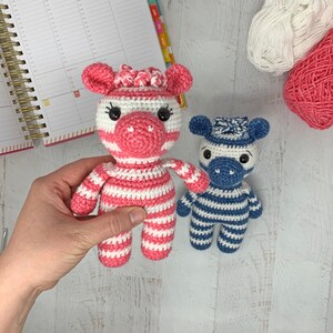 May include: Two crocheted zebra toys. One is pink and white striped and the other is blue and white striped.