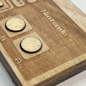 Może przedstawiać: Zbliżenie na drewniany kontroler Nintendo z dwoma okrągłymi przyciskami i wygrawerowanym logo Nintendo na g&oacute;rze.