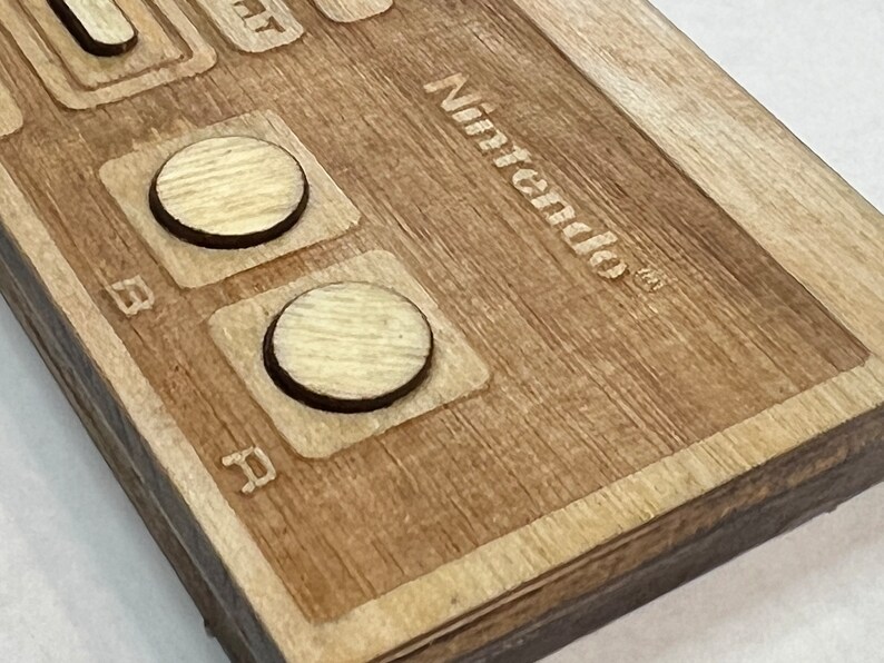 Może przedstawiać: Zbliżenie na drewniany kontroler Nintendo z dwoma okrągłymi przyciskami i wygrawerowanym logo Nintendo na g&oacute;rze.