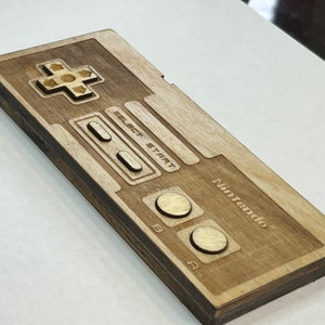 Może przedstawiać: Drewniany kontroler Nintendo z brązowym wykończeniem. Kontroler ma klasyczny design z krzyżakiem, przyciskami i logo Nintendo.