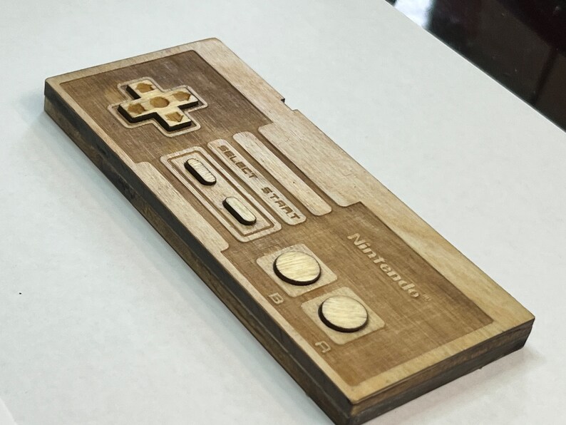 Może przedstawiać: Drewniany kontroler Nintendo z brązowym wykończeniem. Kontroler ma klasyczny design z krzyżakiem, przyciskami i logo Nintendo.