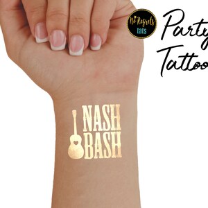 Op de afbeelding: Gouden tijdelijke tattoo met de tekst "I NASH BASH" en een gitaar met een hart erop. De tattoo zit op de pols van een persoon.