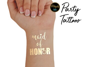 Puede incluir: Tatuaje temporal dorado que dice "dama de honor" con un gráfico de anillo de diamantes. El tatuaje está en la muñeca de una persona.