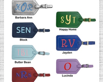May include: Six leather luggage tags with different colored backgrounds and personalized initials. The tags are silver, green, navy blue, light blue, maroon, and purple.
