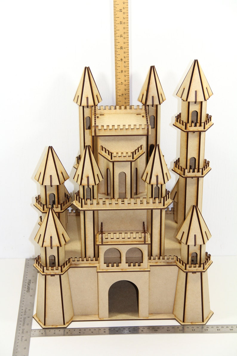 May include: A wooden castle model with multiple towers and a large arched entrance. The castle is made of light brown wood and has brown trim. The castle is about 20 inches tall.
