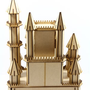 May include: A wooden castle model with a square opening in the front. The castle has multiple towers with crenellations and a brown stain finish.