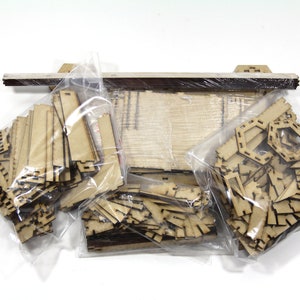 May include: Four plastic bags filled with various wooden pieces for a model building kit. The pieces are cut out and ready to be assembled.