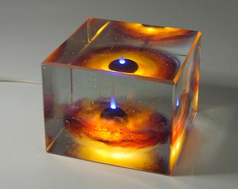 May include: A clear cube with a swirling orange and red nebula inside. Two small black spheres with blue lights are suspended in the nebula.