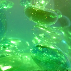 May include: Close-up of a green liquid with round, translucent, green orbs floating inside. The orbs are arranged in a vertical stack, with the top orb partially out of focus.