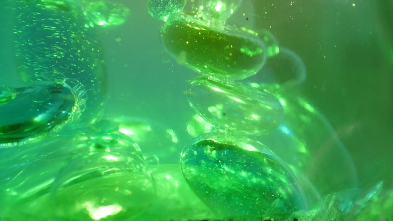 May include: Close-up of a green liquid with round, translucent, green orbs floating inside. The orbs are arranged in a vertical stack, with the top orb partially out of focus.
