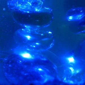 May include: A close-up of a blue glass sculpture with a stack of round, translucent shapes. The sculpture is lit from within, creating a glowing effect.