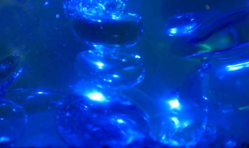 May include: A close-up of a blue glass sculpture with a stack of round, translucent shapes. The sculpture is lit from within, creating a glowing effect.
