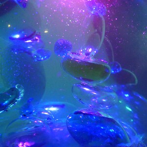 May include: A clear glass orb filled with a blue liquid and iridescent bubbles. The liquid is illuminated from within, creating a shimmering effect.