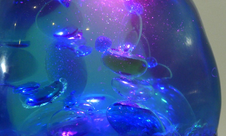 May include: A clear glass orb filled with a blue liquid and iridescent bubbles. The liquid is illuminated from within, creating a shimmering effect.