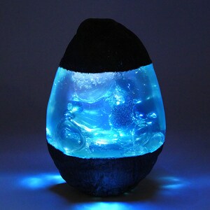 May include: A blue resin egg-shaped lamp with a black base. The lamp is lit and glows blue.