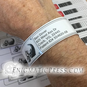 May include: A white wristband with black text and a skull graphic. The text includes a name, address, and patient ID number. The wristband is wrapped around a wrist.