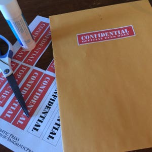 May include: A sheet of paper with multiple red and white "CONFIDENTIAL" stickers. The stickers are arranged in a vertical column. A brown envelope with a red "CONFIDENTIAL OFFICIAL EYES ONLY" sticker is on the right side of the image.