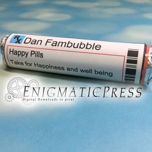 Op de afbeelding: Een zilverfolie-omwikkelde buis met een wit en rood etiket met de tekst "Dan Fambubble Happy Pills Take for Happiness and well being". Het etiket heeft een zwarte barcode en een rood Rx-symbool.