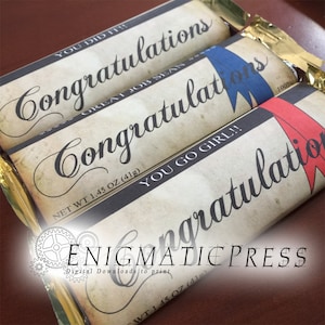 May include: Three wrapped candy bars with the word "Congratulations" in elegant script. Each bar has a different accent color: blue, red, and gold. The bars are labeled with phrases like "You Did It!" and "You Go Girl!!". Each bar is 1.45 oz (41g).