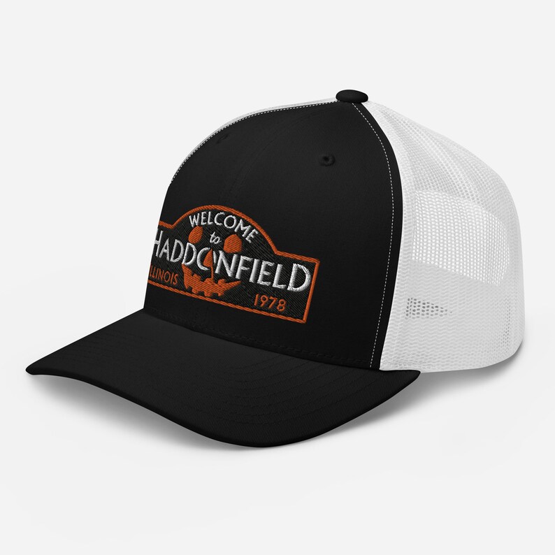 May include: Black and white trucker hat with an orange embroidered patch that says "Welcome to Haddonfield, Illinois 1978". The patch features a jack-o'-lantern face.