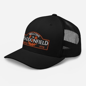 May include: Black trucker hat with a black mesh back. The front of the hat features an embroidered patch that says "Welcome to Haddonfield, Illinois 1978" with a jack-o-lantern face.