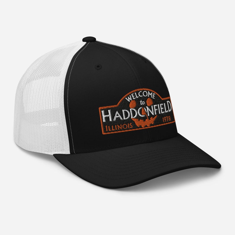 May include: Black and white trucker hat with an orange embroidered patch that says "Welcome to Haddonfield, Illinois 1978". The patch features a jack-o'-lantern face.